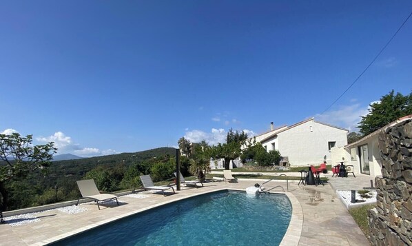 Una piscina con sillas de descanso, un muro de piedra y un edificio con fachada blanca.