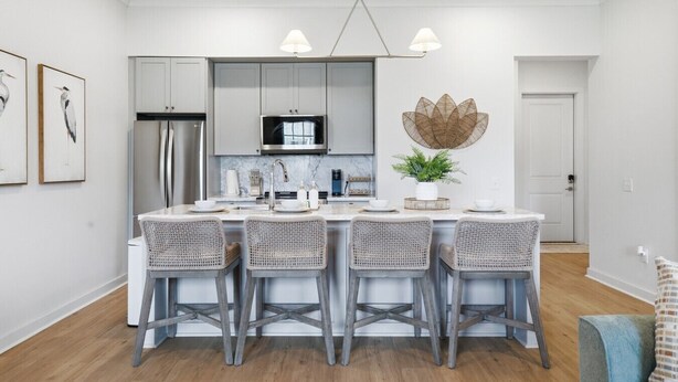 Una cocina moderna con armarios blancos, una isla central con taburetes y una lámpara colgante.