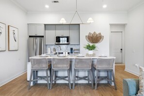 Una cocina moderna con armarios blancos, una isla central con taburetes de bar y una lámpara colgante.