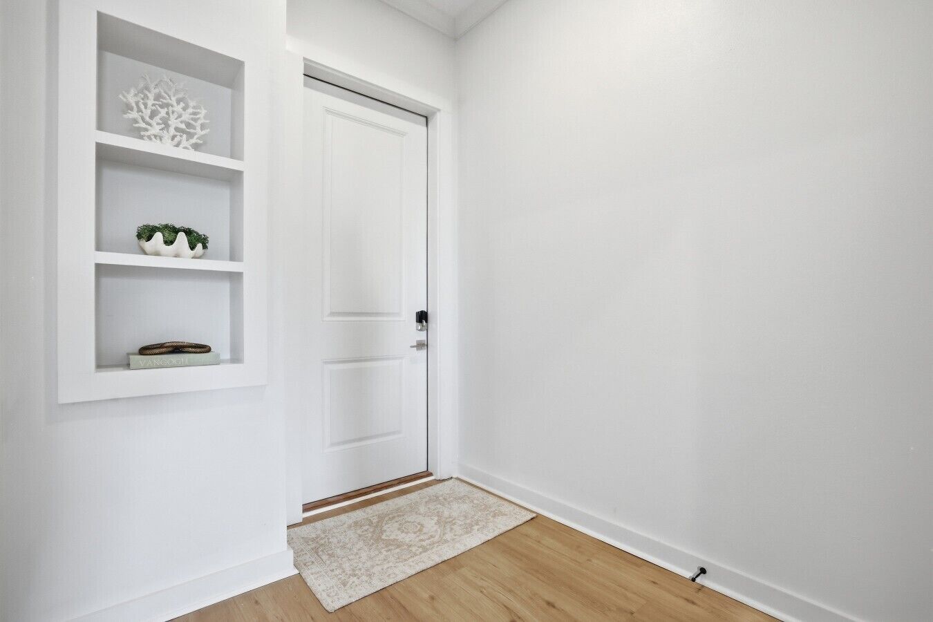 Una puerta blanca con un pequeño estante encima, suelo de madera y pared blanca.
