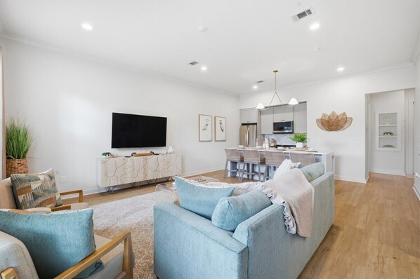 Una sala moderna con sofá, televisor, zona de cocina y comedor.