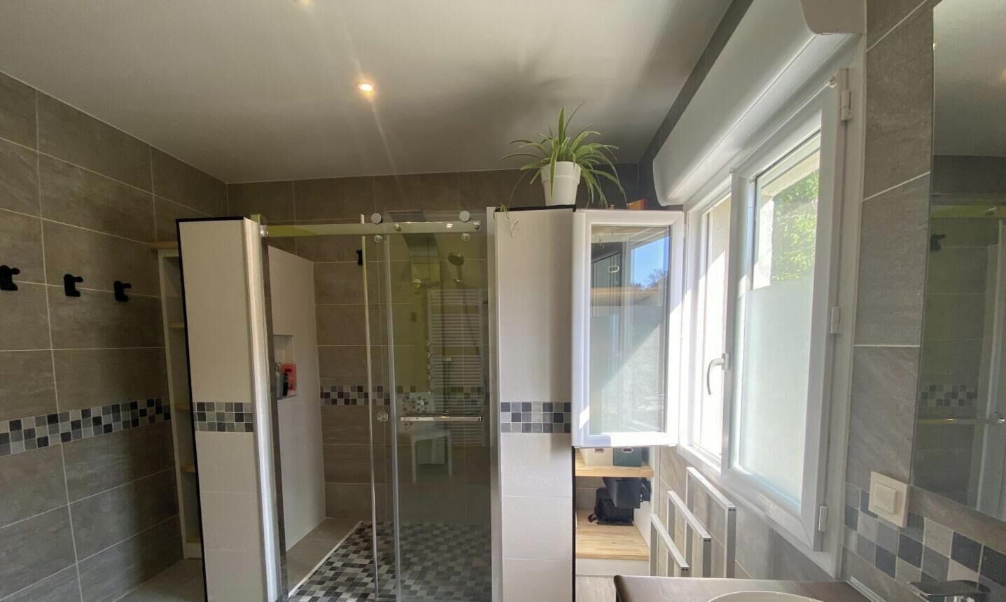 Un baño moderno con cabina de ducha de vidrio, un lavabo blanco y una ventana que proporciona luz natural.