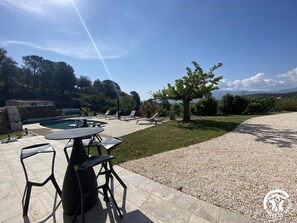 Un espace aménagé au bord de la piscine, avec une table et des chaises, un petit arbre et un ciel dégagé.
