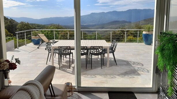 Ein Balkon mit Tisch, Stühlen und einer Sitzecke, mit Blick auf Berge.