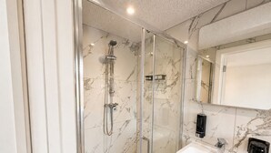 Un baño moderno con ducha envuelta en vidrio, un lavamanos blanco y pared cubierta de mosaicos de mármol.