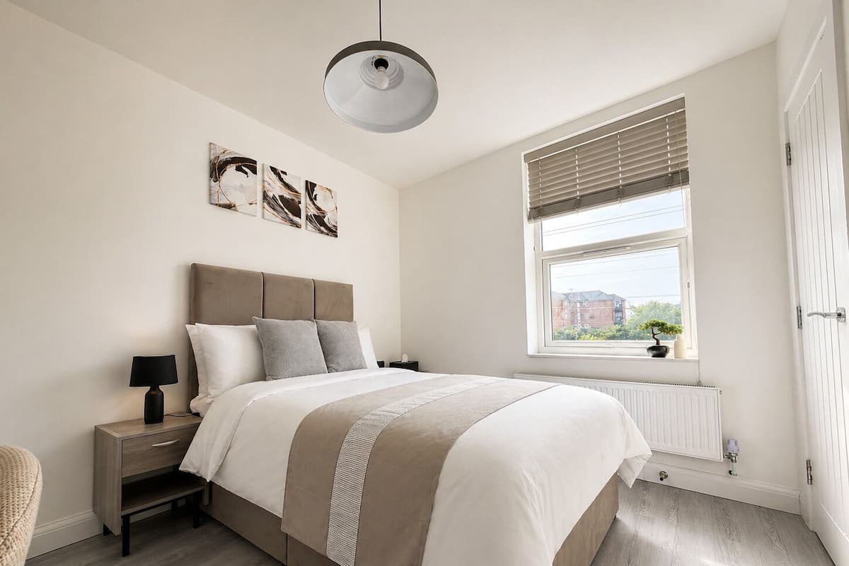 A bedroom with a bed, bedside tables, a window with blinds, and a radiator.