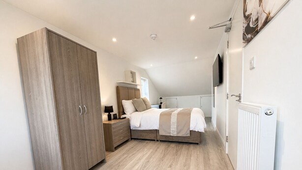 Un dormitorio con cama, mesita de noche, armario y radiador.
