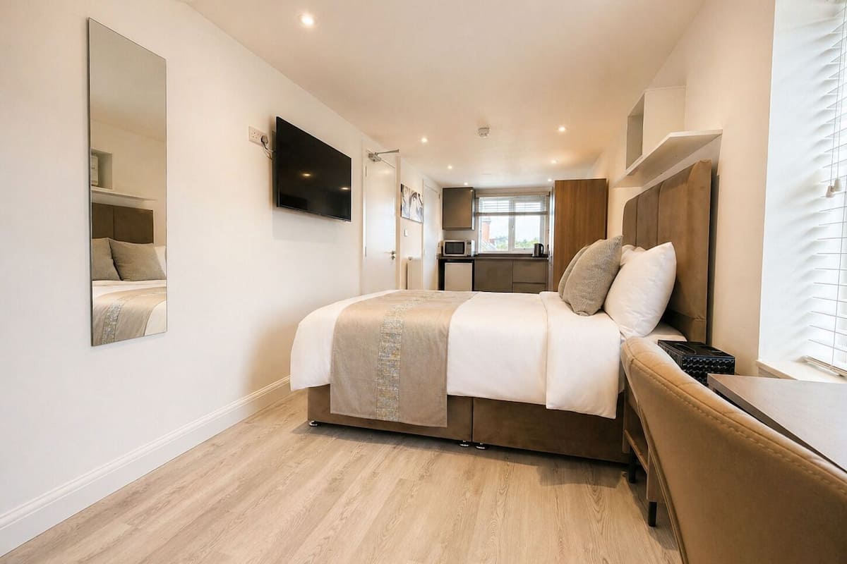 A modern hotel room with a bed, a TV, a small kitchenette, and a bathroom.