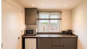 Cocina compacta equipada con microondas, tostadora y hervidor, un refrigerador pequeño y una ventana con vista a una zona residencial.
