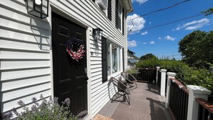 A white house with a black door, a porch with a chair, and a wreath. - New England Coastal Residence (Gloucester)