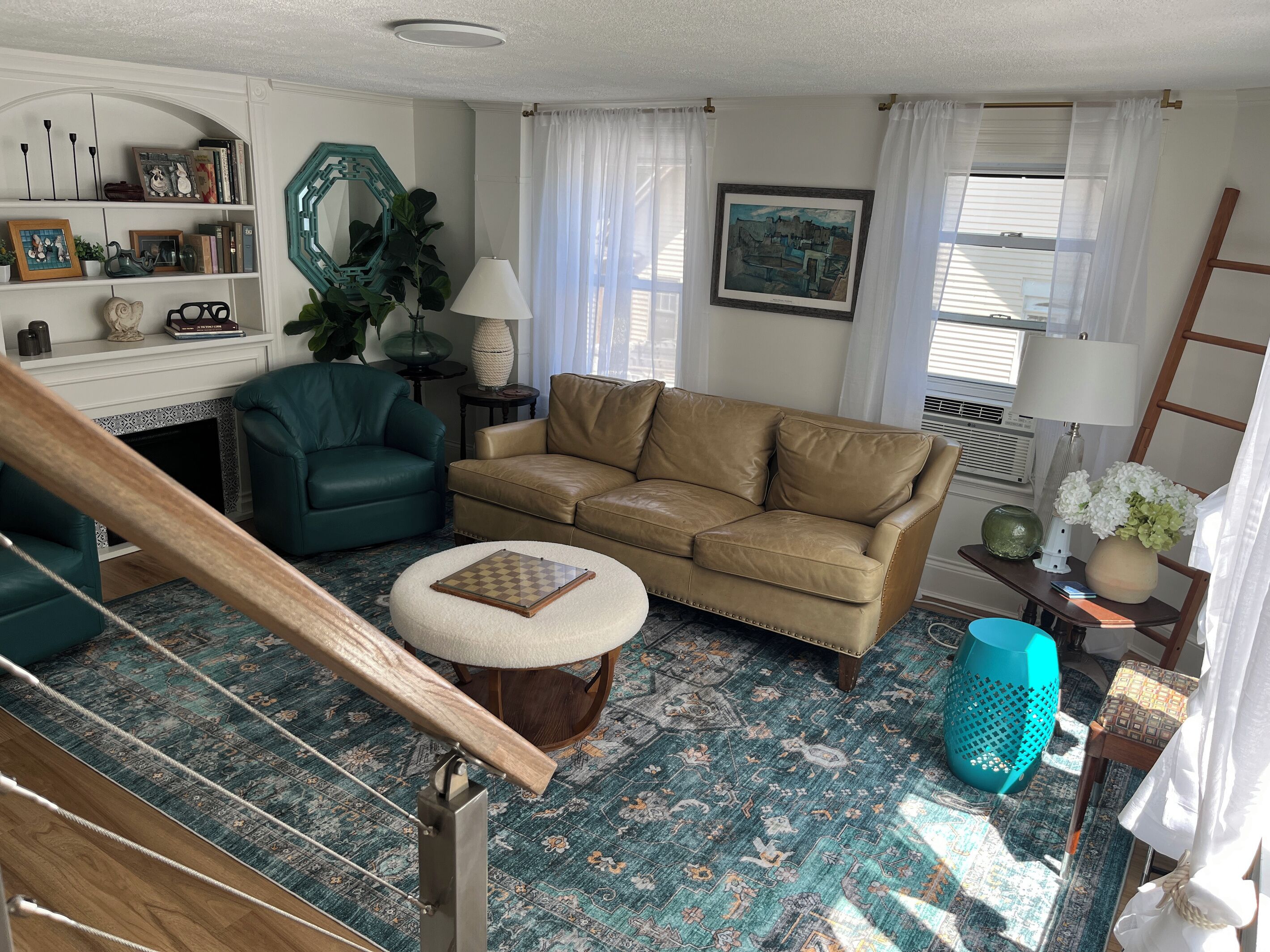 A living room with a green armchair, a tan sofa, a patterned rug, a wooden staircase, and a painting on the wall.