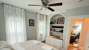 A bedroom with a bed, a ceiling fan, a bookshelf, and a doorway leading to another room. - New England Coastal Residence (Gloucester)