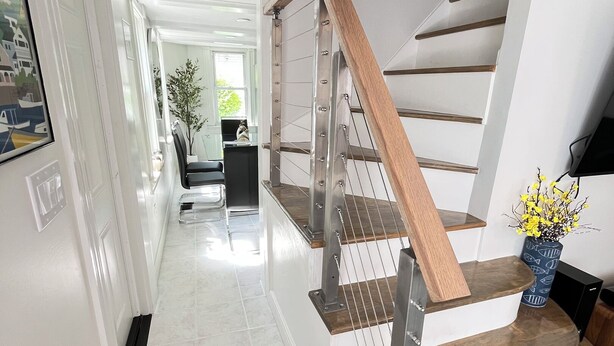 A modern staircase with wooden steps and metal railings, leading to a well-lit interior space. - New England Coastal Residence (Gloucester)