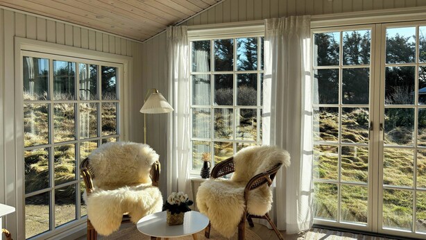Ein Zimmer mit zwei bequemen Sesseln, einem kleinen runden Tisch, einer Lampe und Blick ins Freie durch große Fenster.