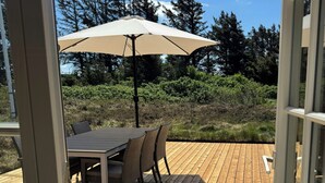 Eine Terrasse aus Holz mit Tisch, Stühlen und Sonnenschirm, mit Blick auf Bäume und Büsche.