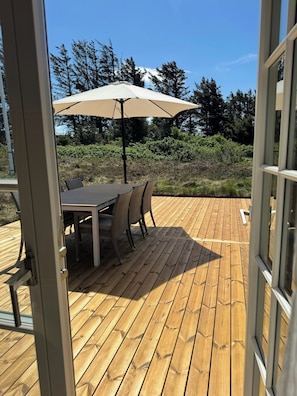 Eine Terrasse aus Holz mit Tisch, Stühlen und Sonnenschirm, mit Blick auf Bäume und Büsche.