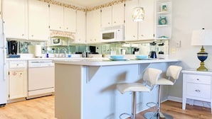 Une cuisine moderne avec des meubles blancs, un îlot central doté de tabourets, un four à micro-ondes et un mixeur.