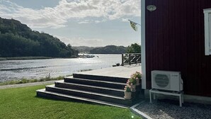 Et hus med en træterrasse, trapper op til en dør, et flag og udsigt til en sø.