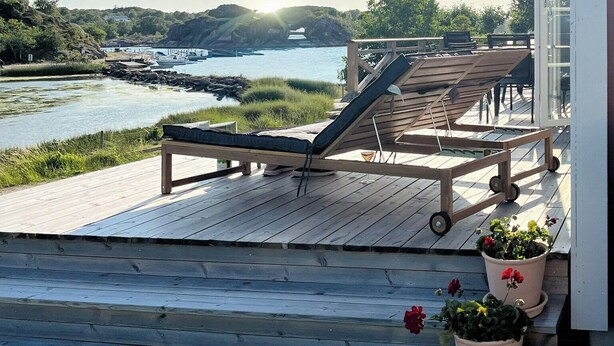 En træterrasse med liggestole, plantekasser og udsigt til et vandareal med både.
