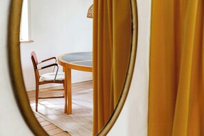 Ein runder Tisch mit einem Stuhl, ein Spiegel, der einen Teil des Raumes widerspiegelt, und ein Fenster mit Tageslicht.