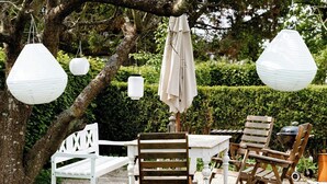 Un'ambientazione in giardino con tavolo e sedie, lanterne appese e una panchina.