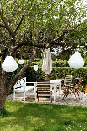 Ein Garten mit Tisch und Stühlen, hängenden Laternen und einer Bank.