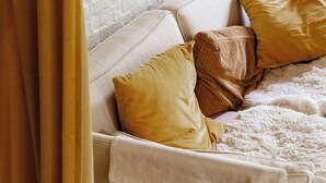 Una stanza con parete in mattoni bianchi, un letto con testiera bianca e un oggetto in legno fissato alla parete sopra il letto.