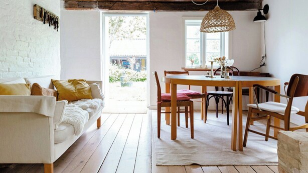 Un accogliente soggiorno con un divano bianco, un tavolo da pranzo in legno e sedie, un lampadario e vista sull'esterno.