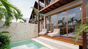 A modern outdoor pool area with stone walls, a wooden deck, and lounge chairs. - Cozy villa, prime Uluwatu, actual walking distance (Badung Regency)