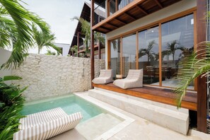 Ein moderner Poolbereich im Freien mit Steinmauern, einer Holzterrasse und Liegestühlen.
