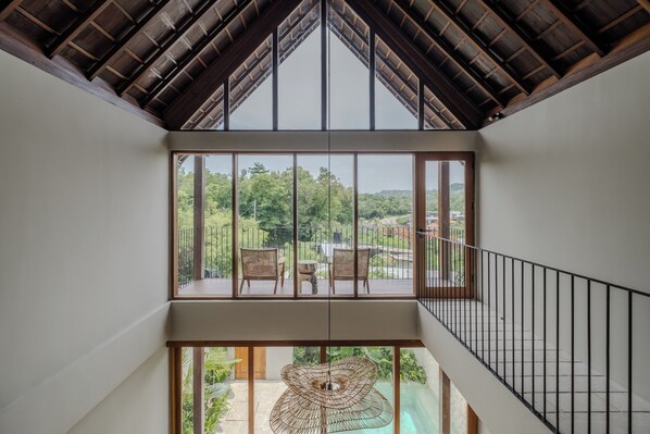 Ein modernes Interieur mit hoher Decke, großen Fenstern und Blick auf Grünfläche.