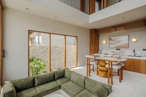 Ein modernes Wohnzimmer mit einer Eckcouch, einem Essbereich mit Tisch und Stühlen sowie einer Küche mit Holzausbau und einer Steinwand.