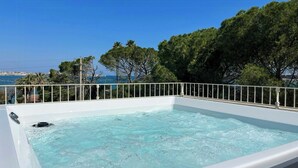 Un jacuzzi con revestimiento blanco, rodeado por una barandilla blanca, con vistas a un cuerpo de agua y follaje.