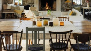 Un loft espacioso con techo alto, vigas de madera a la vista, pared de piedra, chimenea y comedor con sillas y mesa.