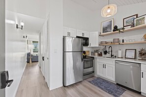A modern kitchen with white cabinets, stainless steel appliances, and a hanging light fixture. - Turtle Bay, Golf Course Views Walk to Beach (Kahuku)