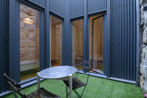 A courtyard with a table and chairs, a stone wall, and a large window. - Cedofeita Hidden Patio (Porto)