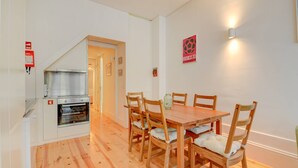 Un comedor con una mesa y sillas de madera, horno empotrado y una lámpara de pared.