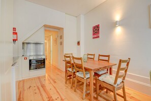 A dining area with a wooden table and chairs, a built-in oven, and a wall-mounted light fixture. - Cedofeita Hidden Patio (Porto)
