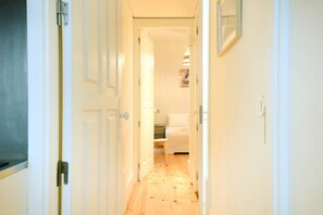 A narrow hallway with white doors, a bed in the distance, and a small table. - Cedofeita Hidden Patio (Porto)