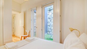Un dormitorio con una cama, una silla, un escritorio y vistas a un jardín a través de una puerta.