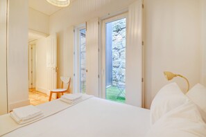 A bedroom with a bed, a chair, a desk, and a view of a garden through a door. - Cedofeita Hidden Patio (Porto)