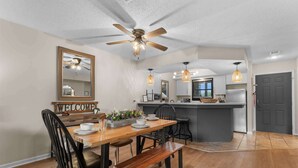 Een moderne keuken met een centraal eiland, een eethoek met een houten tafel en stoelen, en een plafondventilator.