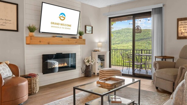 Een woonkamer met een open haard, een televisie, een balkon met buitenmeubilair, en een bord met de tekst 'GRAND WELCOME BRANSON & THE OZARKS'.