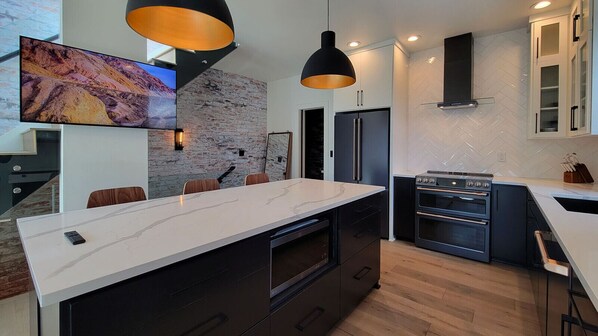 A modern kitchen with a large island, built-in appliances, and a stone accent wall.