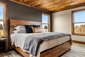 A bedroom with a wooden headboard, a bed with a quilted bedspread, two nightstands, and large windows with a view of trees. - New 2026-MT Views-1 step entry-5 mi to Dolly-Pets (Sevierville)
