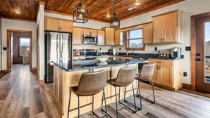 Une cuisine moderne avec des meubles en bois, un réfrigérateur en acier inoxydable, un grand îlot central doté de tabourets de bar et un plafond en bois.