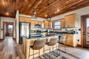 Eine moderne Küche mit Holzschränken, einem Edelstahlkühlschrank, einer großen Kochinsel mit Barhocker und einer Holzbalkendecke.