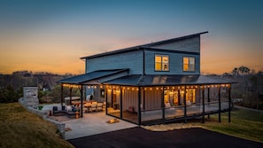 Ein zweigeschossiges Haus mit überdachter Terrasse, Sitzgelegenheit im Freien und einem Whirlpool.