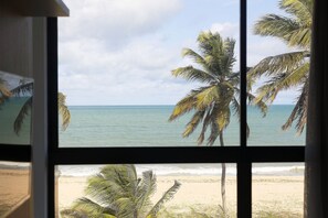 Blick auf einen Strand durch ein Fenster mit Palmen.