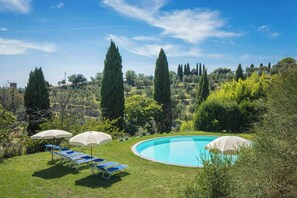 Ein Swimmingpool mit Liegestühlen und Sonnenschirmen, umgeben von Grünpflanzen und Bäumen.